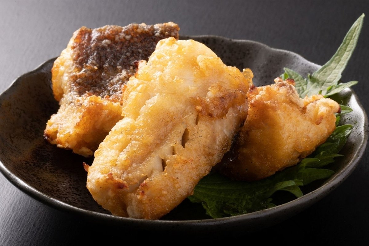 Deep-fried rockfish pieces on shiso leaves in a dark ceramic bowl.