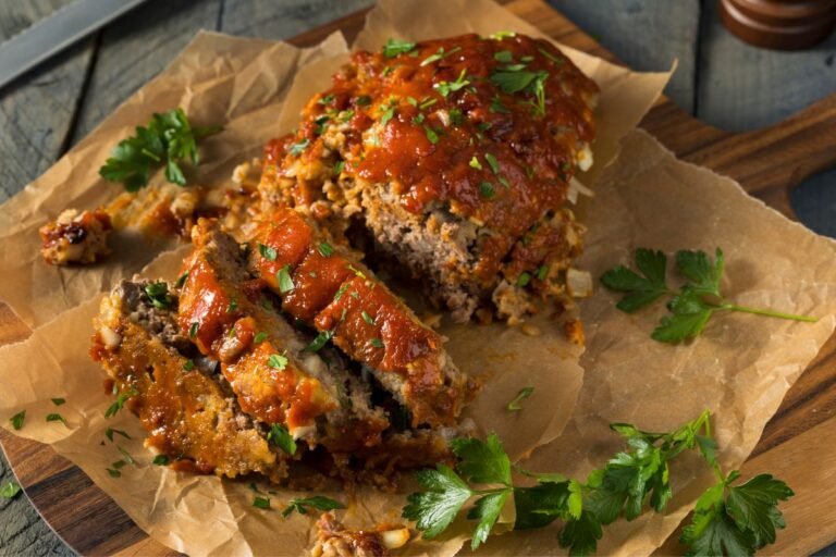 Sliced meatloaf topped with a zesty tomato sauce and fresh parsley, served on parchment paper.