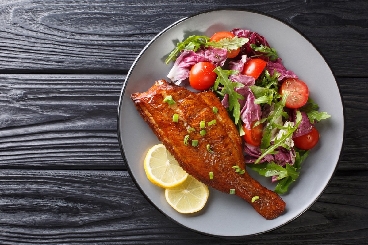 Fried rockfish with a side of mixed green salad and cherry tomatoes on a plate.