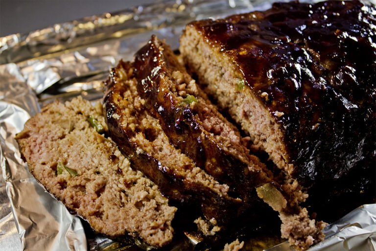 Sliced smoked meatloaf with a shiny barbecue glaze on aluminum foil.