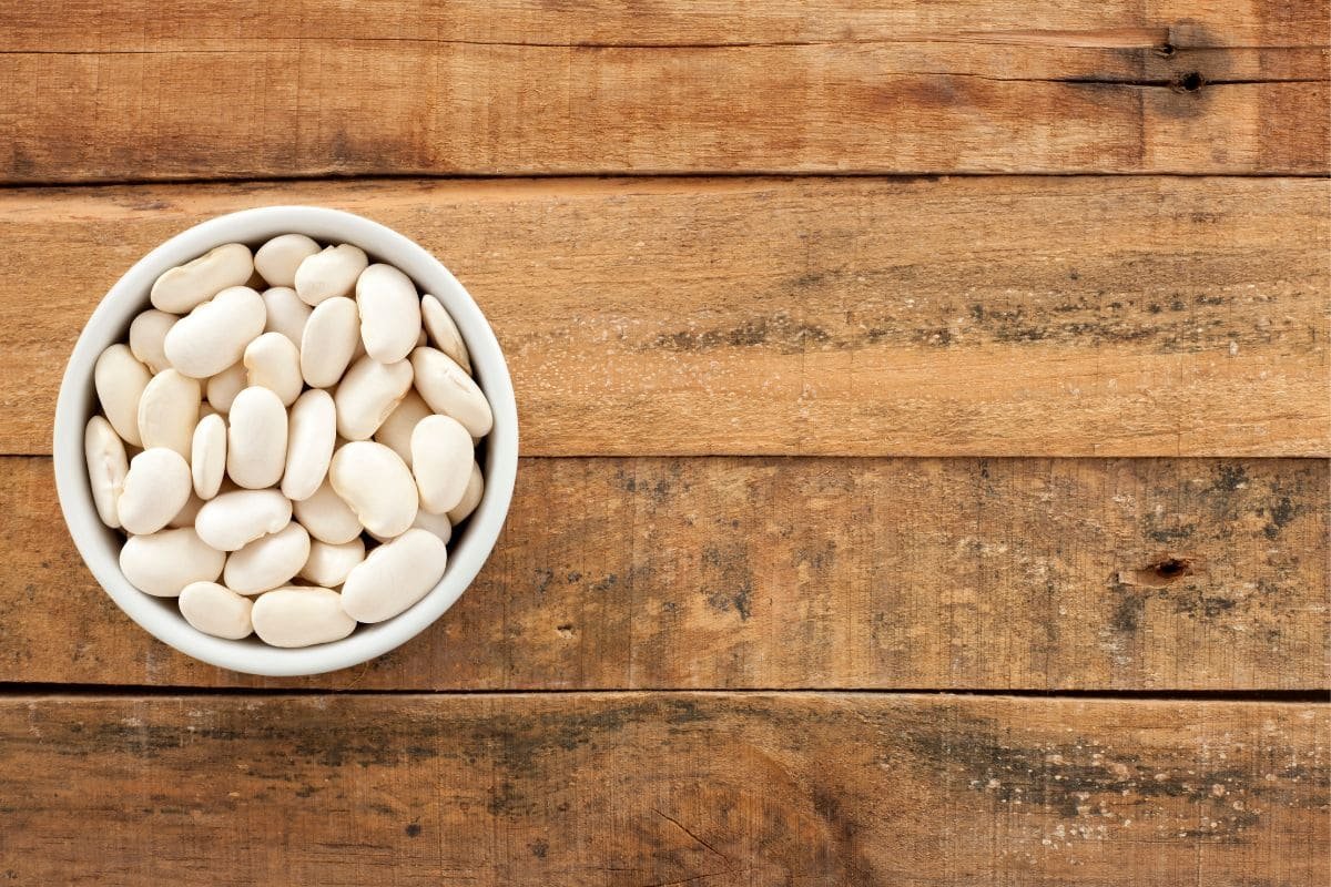 White bowl full of raw butter beans on a rustic wooden table.