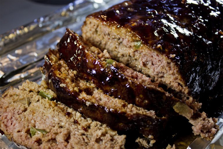 Smoked meatloaf with a glistening glaze, showcasing a rich, caramelized crust and moist, savory interior with visible green peppers and onions.