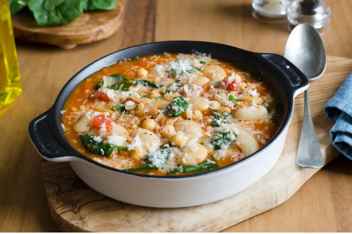 Rustic butter bean soup with spinach and grated cheese in a black cast-iron pot