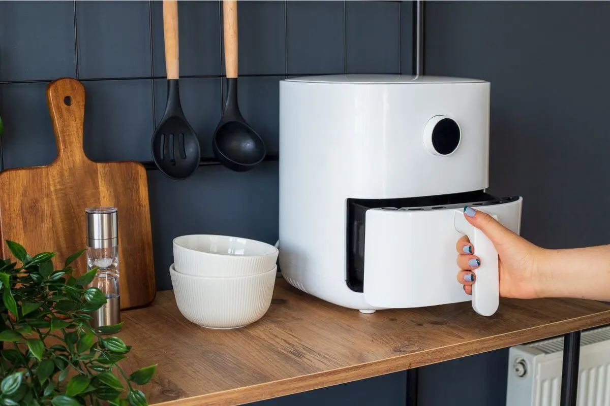 Hand opening a white modern air fryer in a stylish kitchen