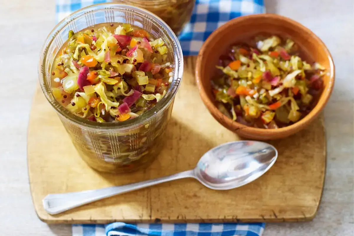 Glass jar and bowl filled with colorful, tangy chow chow relish on a wooden board