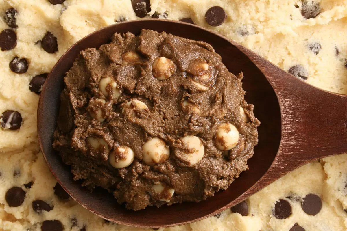  Black cookie dough with white chocolate chips on a wooden spoon