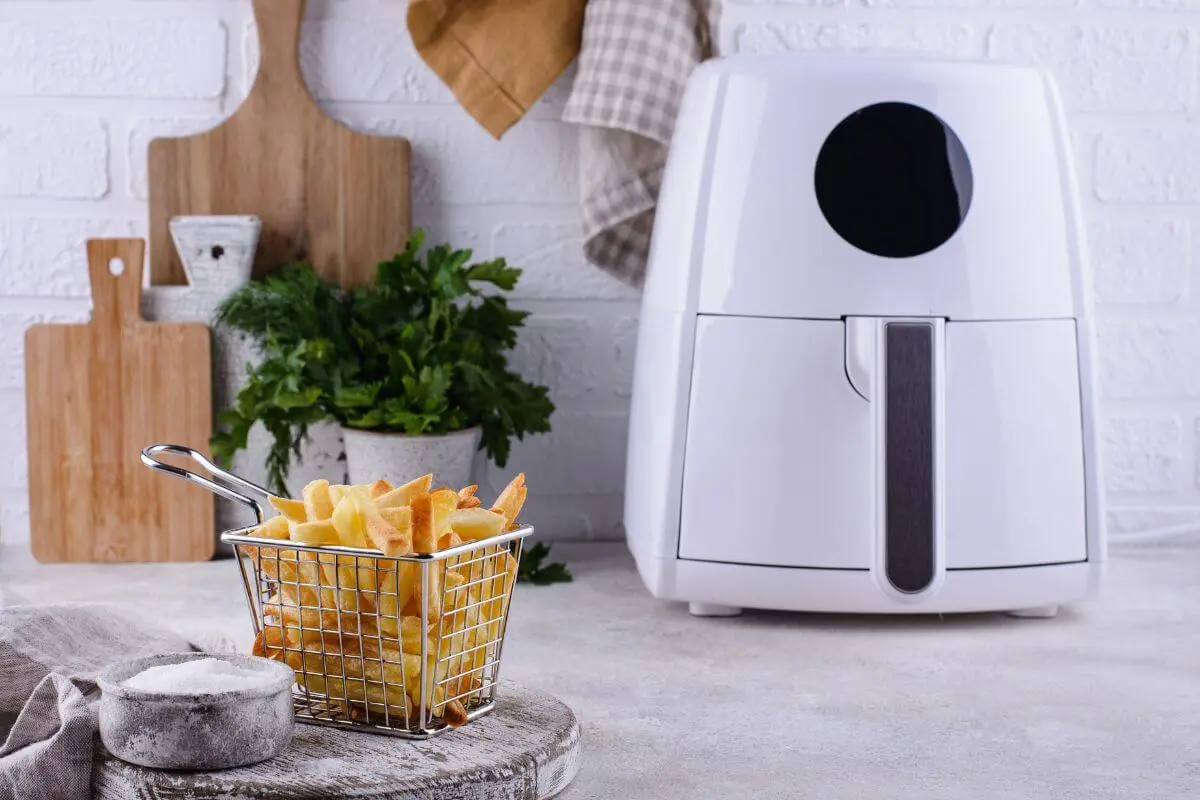 Crispy frozen fries served in a metal basket beside a modern air fryer on a kitchen countertop.