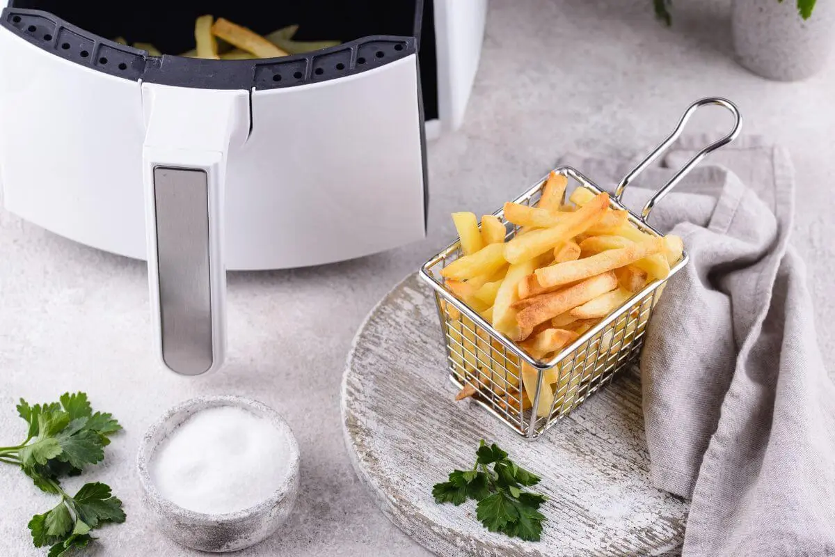 Air fryer with freshly made frozen fries in a serving basket on a kitchen counter.