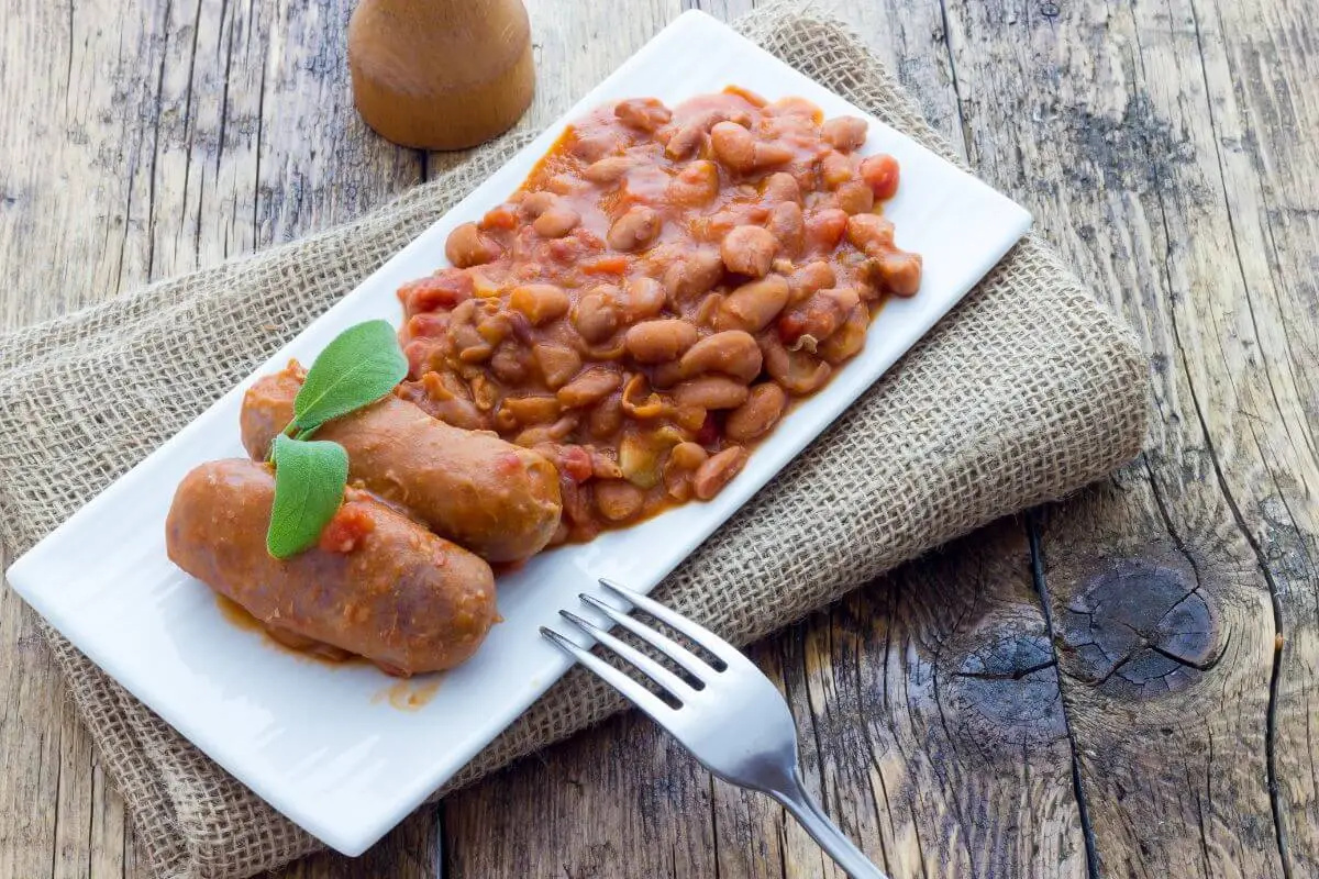 Plate of baked beans with sausage on rustic wooden table