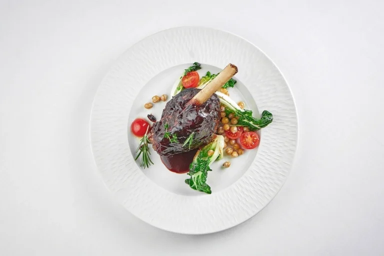 Slow-cooked beef shank with fresh vegetables on a white plate