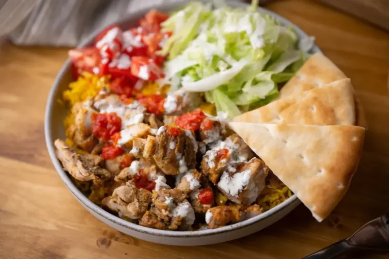 Chicken over rice with lettuce, tomato, and white sauce accompanied by pita bread