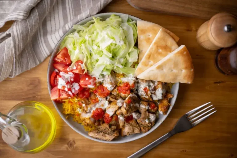 Chicken over rice with white sauce with fresh salad and pita bread on a rustic wooden table