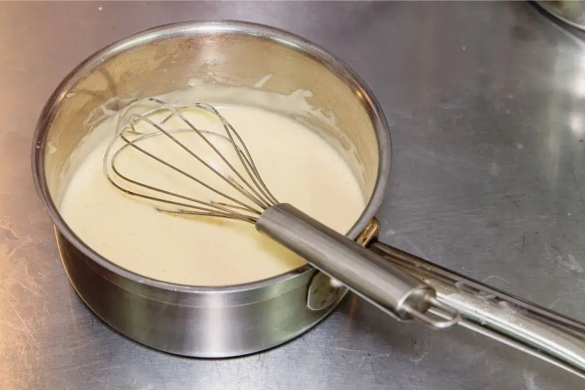 Whisking a creamy white sauce in a stainless steel pot, a key component for chicken over rice