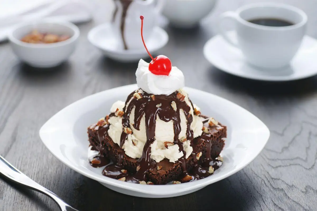 Decadent brownie sundae topped with vanilla ice cream, hot fudge, chopped nuts, and a cherry.