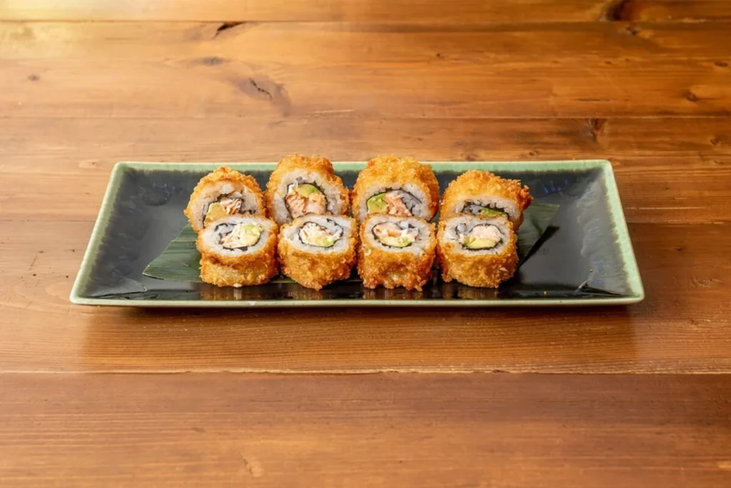 Five pieces of crunchy California roll sushi on a ceramic plate with wooden background.