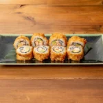 Five pieces of crunchy California roll sushi on a ceramic plate with wooden background.