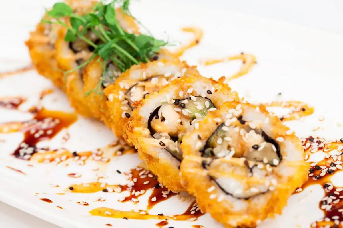 Crunchy California roll sushi topped with sesame seeds and eel sauce on a white plate.