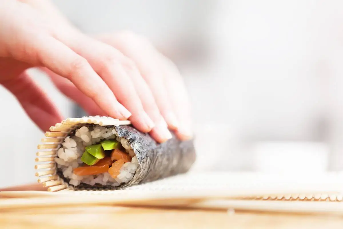 Hand rolling a crunchy California sushi roll filled with avocado and cucumber.